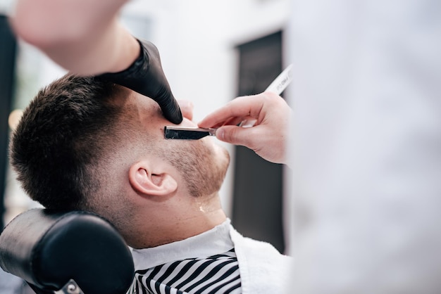 Shave beards in barbercos. Men's haircut and facial care. Barber makes a haircut to the client.