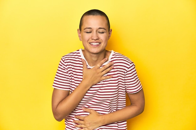 Shaved head woman in red striped tee yellow backdrop laughs happily