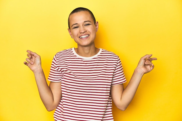 Shaved head woman in red striped tee yellow backdrop pointing to different copy spaces choosing one