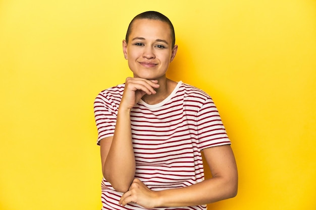 Shaved head woman in red striped tee yellow backdrop smiling happy and confident