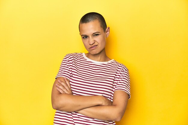 Shaved head woman in red striped tee yellow backdrop unhappy looking in camera
