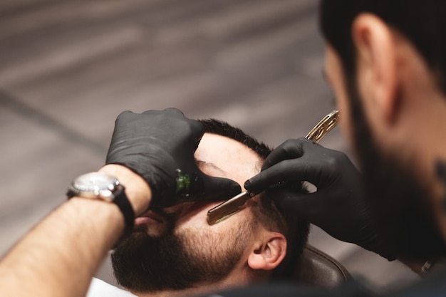 Shaving a beard in a barbershop with a dangerous razor. Barber Shop Beard Care. Drying, cutting, cutting a beard. 