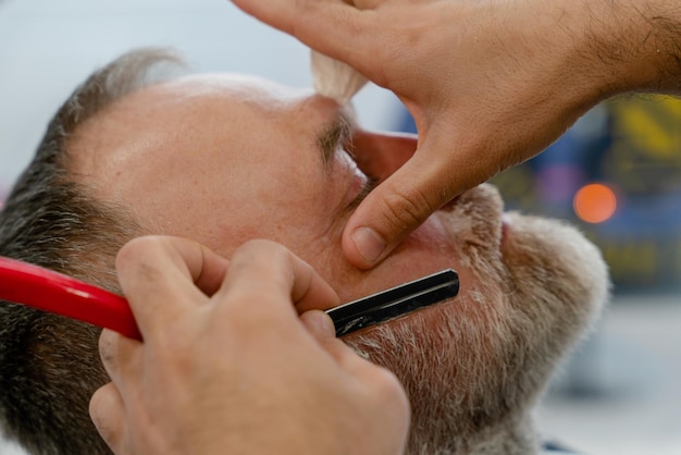 Shaving with a straight razor in a barbershop A bearded old man being shaved in a barbershop