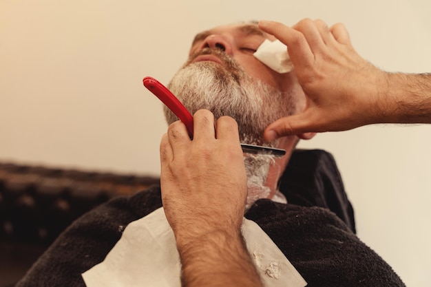 Shaving with a straight razor in a barbershop A bearded old man being shaved in a barbershop