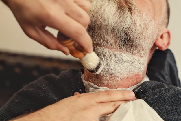 Shaving with a straight razor in a barbershop A bearded old man being shaved in a barbershop