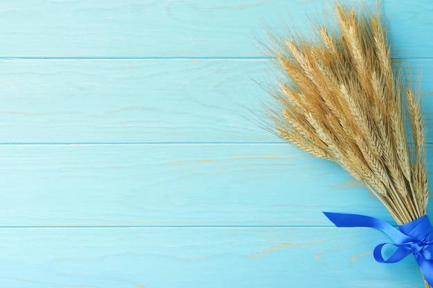 シャブオットのユダヤ人の祝日のお祝い青いリボンと金色の熟した小麦の花束小麦畑と白い木の板のテーブルシャブオットのお祝いの背景トップ ビュー モックアップ
