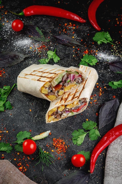 Shawarma burrito cut with vegetables and herbs on a dark stone table The concept of fast food restaurants