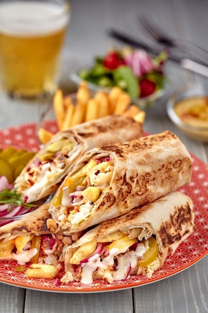 Shawarma chicken roll in a pita with fresh vegetables cream sauce and french fries on wooden backgro...