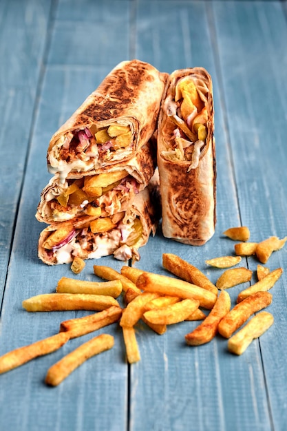 Shawarma chicken roll in a pita with fresh vegetables cream sauce and french fries on wooden backgro...