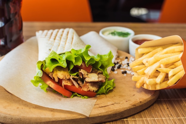 Shawarma and french fries on a wooden board in a restaurant. Tortilla with a drink in a cafe.