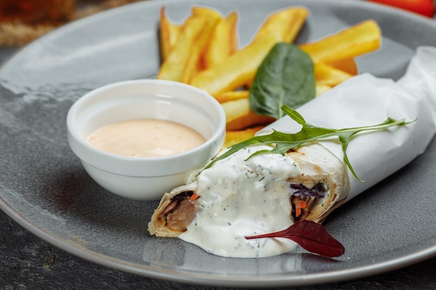 Shawarma sandwich with french fires and salt grinder on dark background