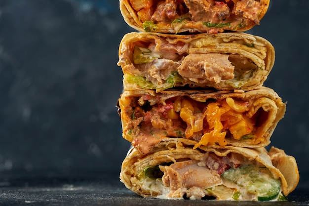 Shawarma stacked one on top of the other with meat and vegetable filling. A stack of shawarma on a dark background. Selective focus