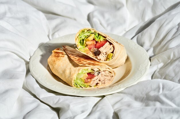 Photo shawarma with chicken and vegetables in a plate on a white sheet hard light