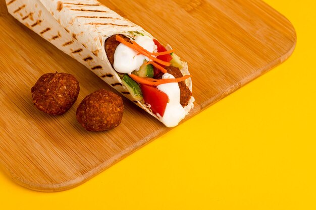 Shawarma with falafel on a wooden board side view on a yellow background