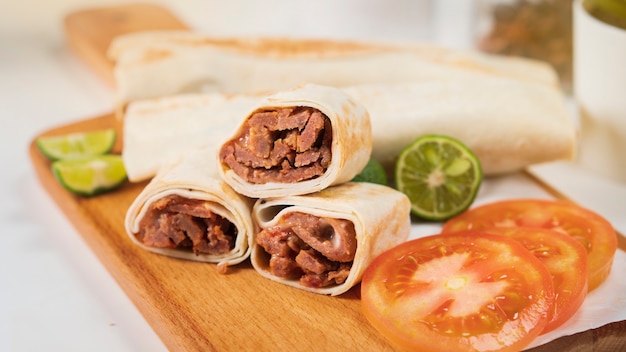 Shawarma with meat, mayonnaise, tomato and lime on a wooden cutting board