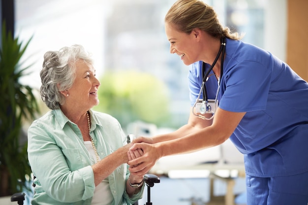 Она прекрасно ладит со своими пациентами. Снимок врача, пожимающего руку улыбающейся пожилой женщине, сидящей в инвалидной коляске.