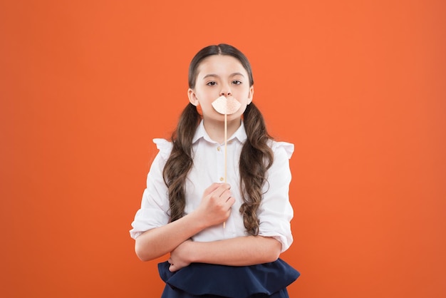 She is really cute happy childhood small girl student school girl in uniform child with party lips smart and intelligent kid on orange background back to school knowledge day kid fashion