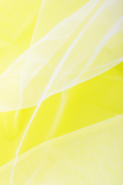 Sheer tulle fabric arranged in soft folds on a yellow background selective focus