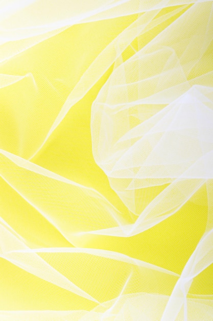 Sheer tulle fabric arranged in soft folds on a yellow background selective focus