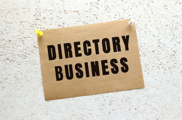 버튼이있는 흰색 질감 벽에 DIRECTORY BUSINESS 텍스트가 부착 된 공예 용지