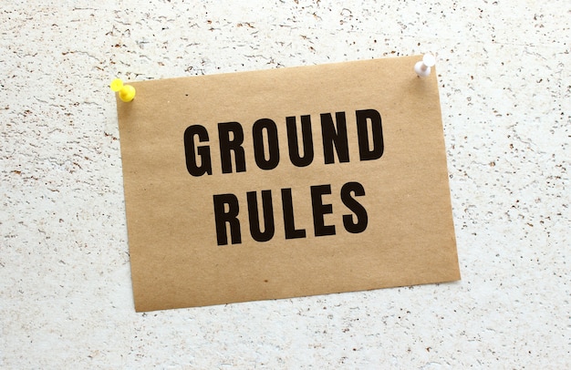 버튼이 있는 흰색 질감 벽에 GROUND RULES 텍스트가 첨부된 공예 용지. 사무실 알림입니다.