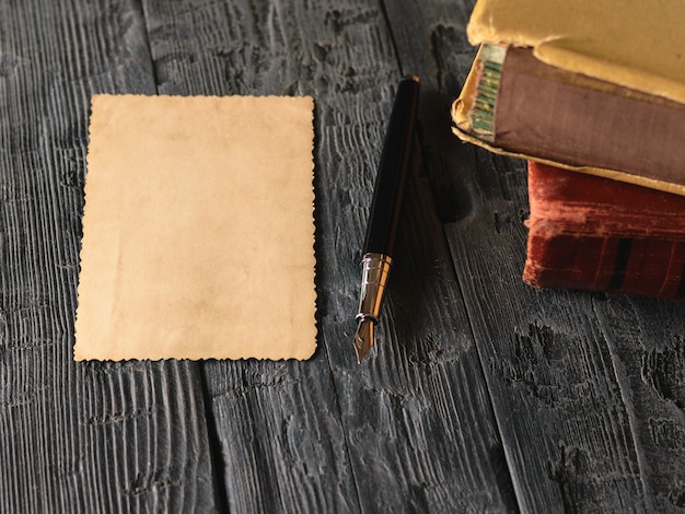 A sheet of old paper and a fountain pen with books on a wooden table. Retro writing paper.