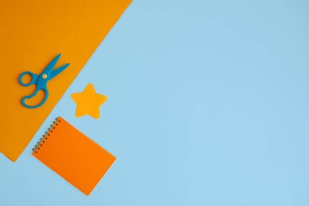 A sheet of orange paper with scissors, an orange Notepad, and a star-shaped sticker on a blue background. Flat layout with copy space