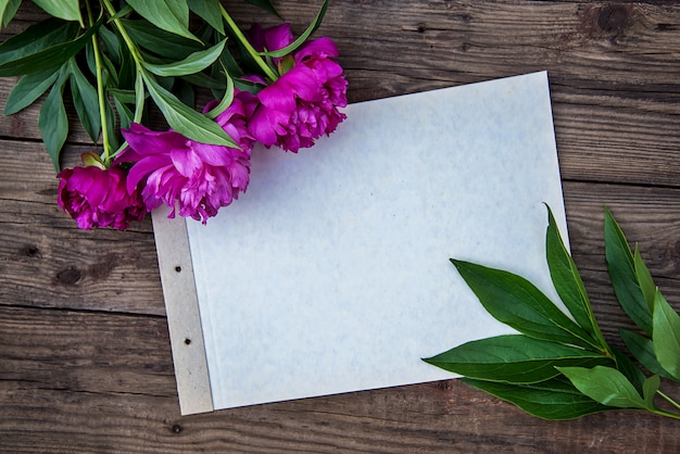 Foto un foglio di carta e alcune peonie rosa su fondo in legno con copia spazio come una cartolina