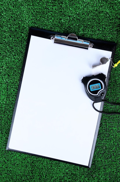 Sheet of paper stopwatch and whistle on grass closeup