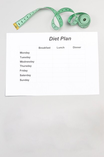 Foto un foglio di carta con il piano di dieta per la settimana due ciotole di riso il nastro di misurazione su grigio.