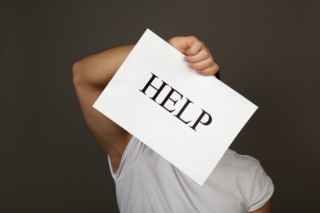 Sheet of paper with Help sign in male hand on dark wall