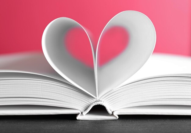 Sheets of book curved into heart shape on pink background