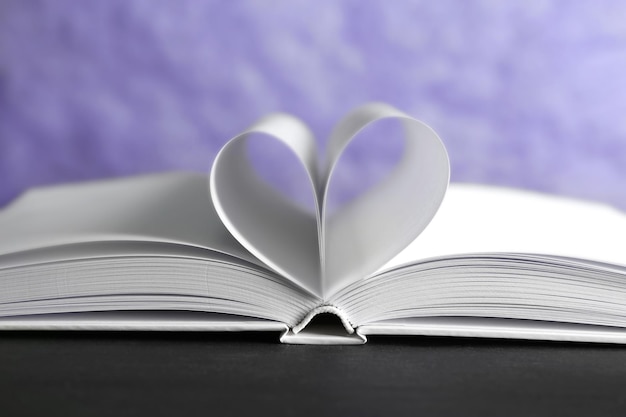 Листы книги изогнуты в форме сердца на несфокусированном синем фоне