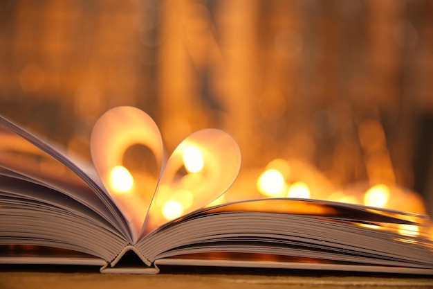 Sheets of book curved into heart shape on wooden table against unfocused lights