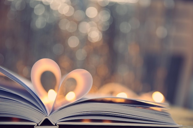 Sheets of book curved into heart shape on wooden table against unfocused lights