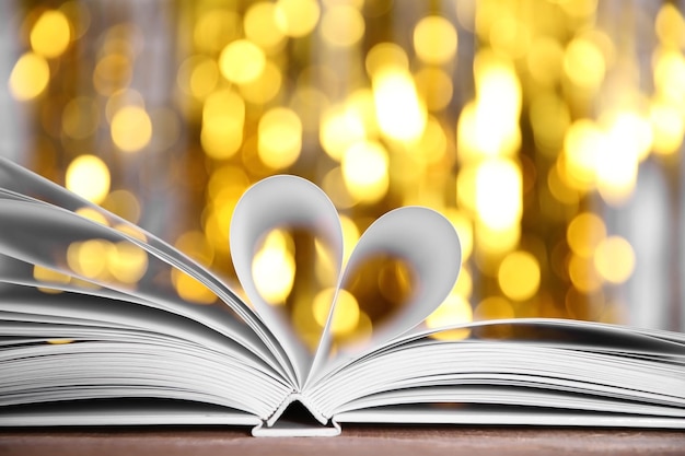 Sheets of book curved into heart shape on wooden table against unfocused lights