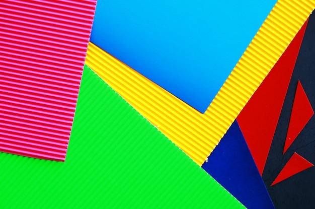 Листы цветной бумаги, переливающаяся палитра цветной бумаги, цвета радуги. Вид сверху на стол с цветной бумагой и ножницами.