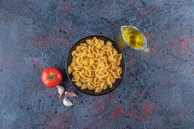 Shell ongekookte pasta in een glazen kom met verse rode tomaat en knoflook.