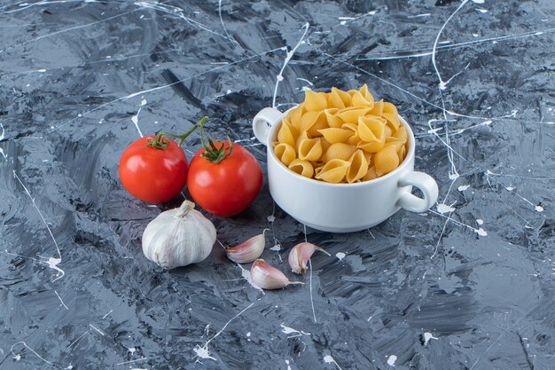 Shell uncooked pasta in a bowl with fresh red tomatoes and garlic . 