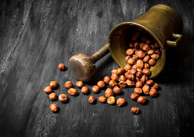 Shelled hazelnuts in an old mortar and pestle. On the black wooden table.