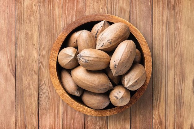 Shelled pecan nuts raw in bowl on wooden table background top view organic vegetarian food