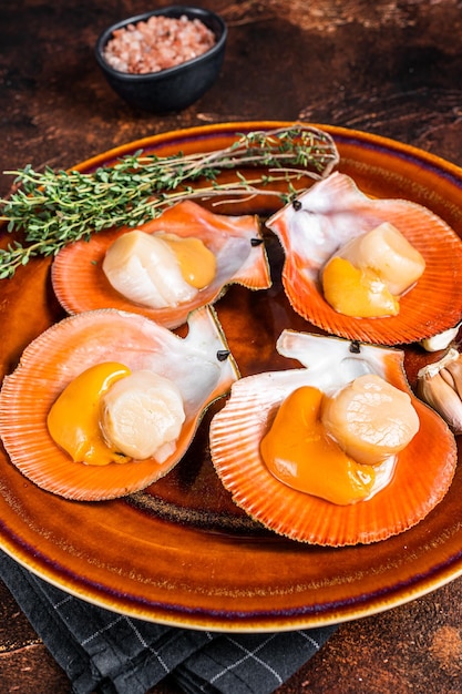 Shellfish raw Scallops on a rustic plate with thyme. Dark background. Top view.