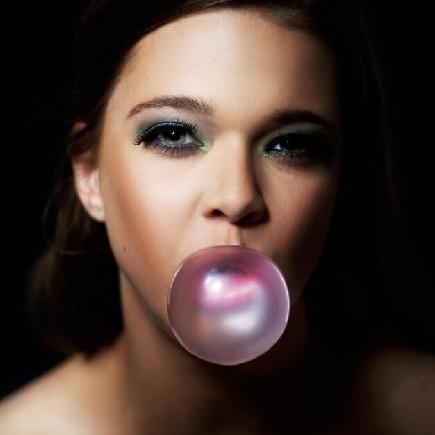 Shes got plenty of attitude Shot of a young woman blowing a bubble with her gum against a dark background