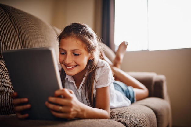 Shes so techsavvy Full length shot of a young girl using her tablet while lying on a sofa at home