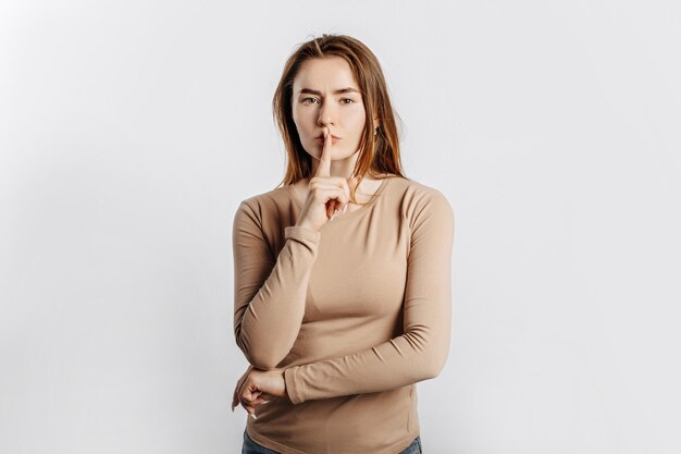 Shh gebaar. Mooi meisje fronsen en met een vinger op haar lippen op grijze achtergrond