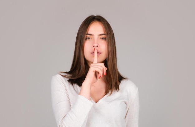 Shh womens secrets Woman showing secret sign Female with finger in mouth Closeup portrait of young woman is showing a sign of silence with shhh