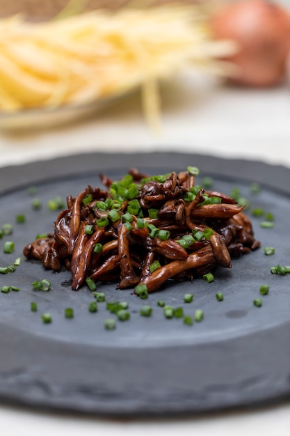 Shimeji mushroom served with chives on black stone plate. Typical oriental meal. Detail of food dish, closeup, selective focus.