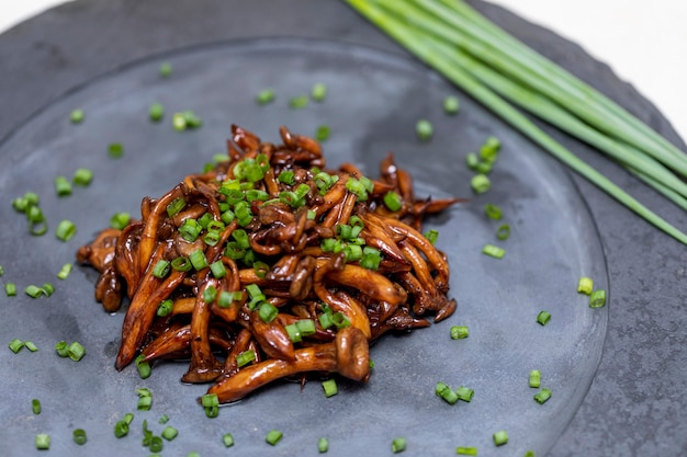 Shimeji mushroom served with chives on black stone plate. Typical oriental meal. Detail of food dish, closeup, selective focus.