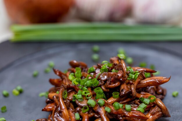 Photo shimeji mushroom served with chives on black stone plate. typical oriental meal. detail of food dish, closeup, selective focus.