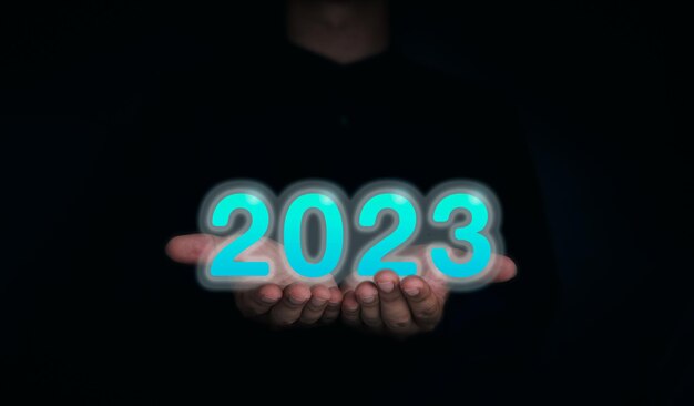 Shining en glow blue 2023 jaarkalender De 2023-nummers op de handen van de zakenman op donkere achtergrond voor digitaal en technologisch concept Welkom prettige kerstdagen en gelukkig Nieuwjaar banner